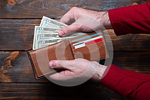 Wallet with dollars in men`s hands. Wallet with money and credit cards on a wooden background