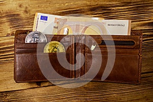 Wallet with fifty euro bills and bitcoins on wooden background