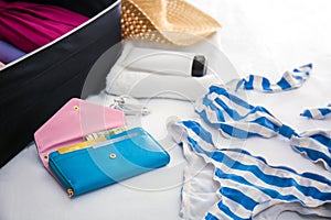 Wallet, swimsuit and open suitcase with packed things on bed