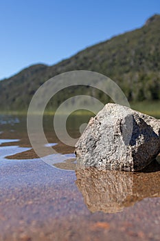 Wallpaper of isolated gray strone in transparent lake water with a huge mountain with forests and a clear sky in Lago Falkner,