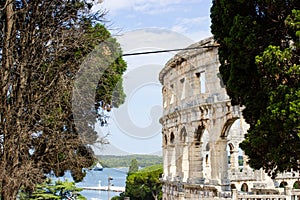 Walls of the Pula Arena, the only remaining Roman amphitheatre entirely preserved, between some trees in Pula, Croatia, with