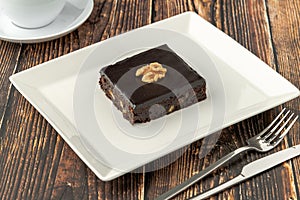 Walnut and dark chocolate brownie on a white porcelain plate on wooden table