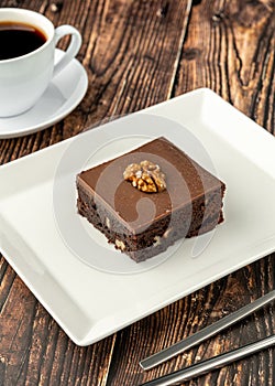 Walnut and dark chocolate brownie on a white porcelain plate on wooden table