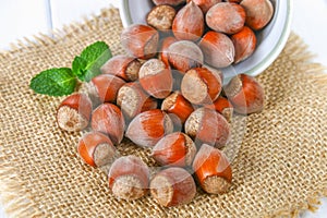 Walnut hazelnuts scattered on sackcloth on a white wooden table.