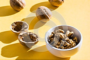 Walnut kernels in a bowl and walnut shells on a yellow table