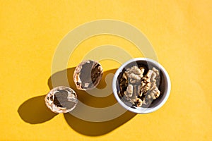 Walnut kernels in a bowl and walnut shells on a yellow table