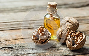 Walnut oil in glass of bottle, whole big peeled walnut kernel with thin shell on wooden background
