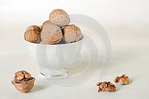 Walnut in a shell are stacked in a white cup. Next peeled nuts. Vegetable protein is an analogue of animal. Light background