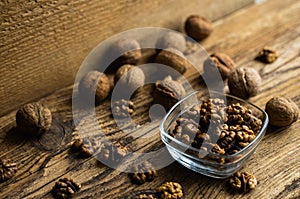 Walnut in a smale plate with scattered shelled nuts and whole nut which standing on a wooden vintage table. Walnuts is a