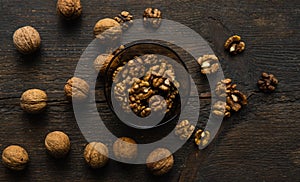 Walnut in a smale plate with scattered shelled nuts and whole nut which standing on a wooden vintage table. Walnuts is a