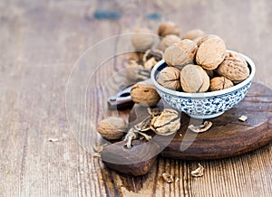 Walnuts in ceramic bowl and on cutting board with nutcracker over rustic wooden background