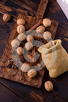 Walnuts, cinnamon, star anise, coffee beans, and small bag on wooden cutting board. Nuts and spices on the table. Food