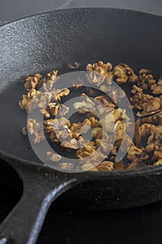 Walnuts cooking in a cast iron frying pan on a ceramic hob