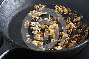 Walnuts cooking in a cast iron frying pan on a ceramic hob