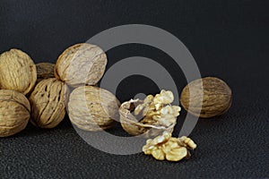 Walnuts lie in a heap on a dark background, one is split, half the shell and a delicious kernel.
