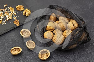 Walnuts in a reusable bag. Nut shells on the table, nut kernels on a black stone board