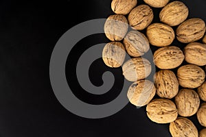 Walnuts in shell on black surface, top view. Background of round walnuts. Healthy nuts and seeds composition.