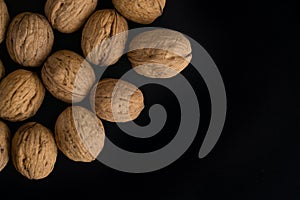 Walnuts in the shell on black surface, top view. Background of round walnuts. Healthy nuts and seeds composition.