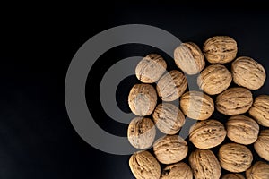 Walnuts in shell on black surface, top view. Background of round walnuts. Healthy nuts and seeds composition.