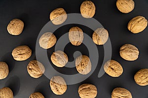 Walnuts in the shell on black surface, top view. Background of round walnuts. Healthy nuts and seeds background.