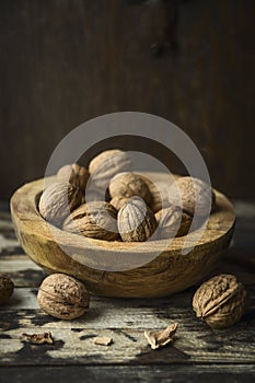 Walnuts with and without shell in a rustic bowl on kitchen table over wooden background