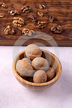 Walnuts in wooden bowl and on wooden carved board on bright textured surface. Healthy nuts and seeds composition.