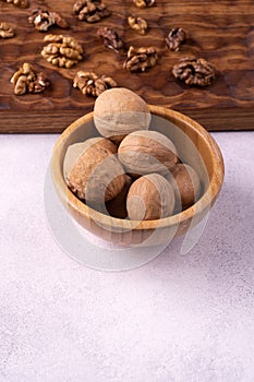 Walnuts in wooden bowl and on wooden carved board on bright textured surface. Healthy nuts and seeds composition.