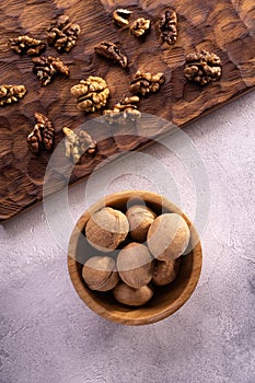 Walnuts in wooden bowl and on wooden carved board on bright textured surface. Healthy nuts and seeds composition.