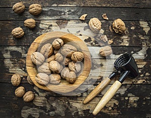 Walnuts in a wooden bowl on a wooden rustic background with tongs for cracking nuts,top view photo