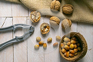 Walnuts in a wooden box next to a hazelnut in a coconut shell, nuts scattered on a white wooden table on which the nut cracker