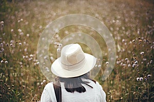 Wanderlust and travel concept. Hipster girl with backpack traveling in sunny mountains, walking in  wildflower meadow. Stylish