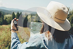 Wanderlust and travel concept. Stylish hipster girl holding map and compass, traveling in sunny mountains. Woman in hat exploring