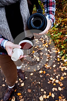 Wanderlust and Travel concept. Woman pouring a hot drink in mug from thermos. Drinking tea outdoors