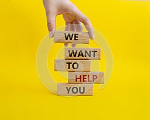 We want to help you symbol. Wooden blocks with words We want to help you. Beautiful yellow background. Businessman hand. Business