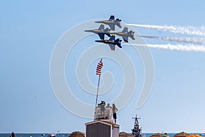 Four US Navy Blue Angels Jets flying in formation over a lifeguard stand at the beach during an airshow