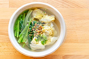 Wanton soup with morning glory and deep fried garlic in bio paper bowl on wooden background