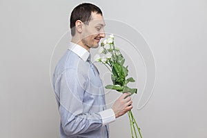 He wants to give a flowers. Side view portrait of charming pleasure romantic young man in blue shirt holding bouquet of white flow