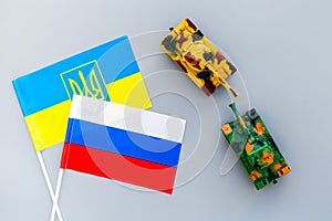 War, confrontation concept. Russia, Ukraine. Tanks toy near russian and Ukrainianflag on grey background top view