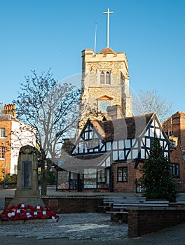 War Memorial with wreaths of red poppies at the foot, with historic Tudor building and Pinner Parish Church behind. Pinner UK