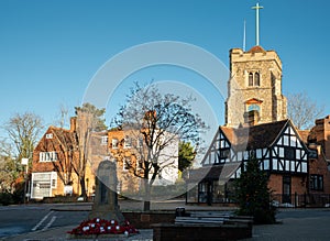 War Memorial with wreaths of red poppies at the foot, with historic Tudor building and Pinner Parish Church behind. Pinner UK