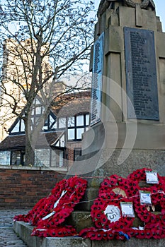 War Memorial with wreaths of red poppies at the foot, with historic Tudor building and Pinner Parish Church behind. Pinner UK