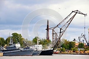 War ship and tug boat in port near crane