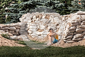 War in Ukraine. A girl sits on sandbags near her house. This building was made for the defense of the city.