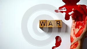 War word made of wooden cubes, bleeding hand on table, political conflict