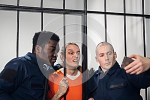 Wardens in a maximum security prison take selfies with a prisoner with tattoos on his face, who is sitting in a cell.