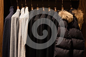 wardrobe with men's clothes in dark colors. jacket, down jacket, shirt. The clothes are neatly hung on wooden