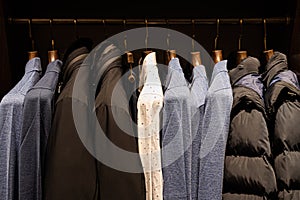 wardrobe with men's clothes in dark colors. jacket, down jacket, shirt. The clothes are neatly hung on wooden