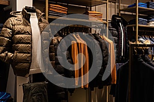 wardrobe with men's clothes in dark colors. jacket, down jacket, shirt. The clothes are neatly hung on wooden