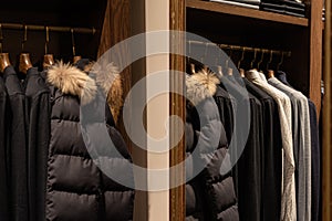wardrobe with men's clothes in dark colors. jacket, down jacket, shirt. The clothes are neatly hung on wooden