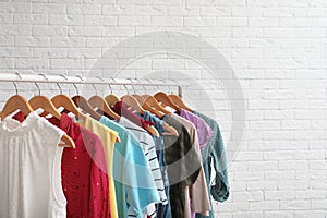 Wardrobe rack with stylish clothes near brick wall indoors.